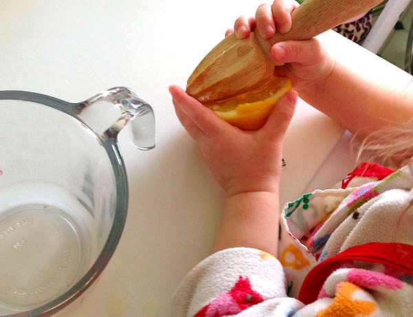 two year old baby hands squeezing a lemon with wood citrus reamer