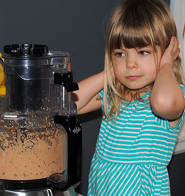 three year old girl covering her ears with food processor blending hummus