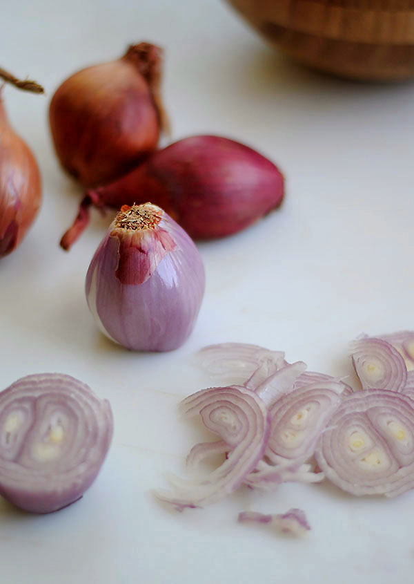 chopped red shallot rings on counter in front of whole shallots and a bowl