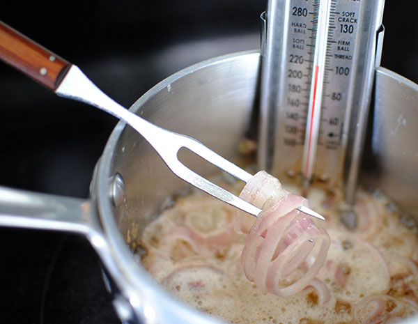 Lifting shallot rings with a fork out of oil with thermometer showing 220° 