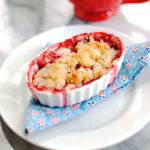 individual strawberry rhubarb crumble on a blue floral napkin lined plate and cup of coffee