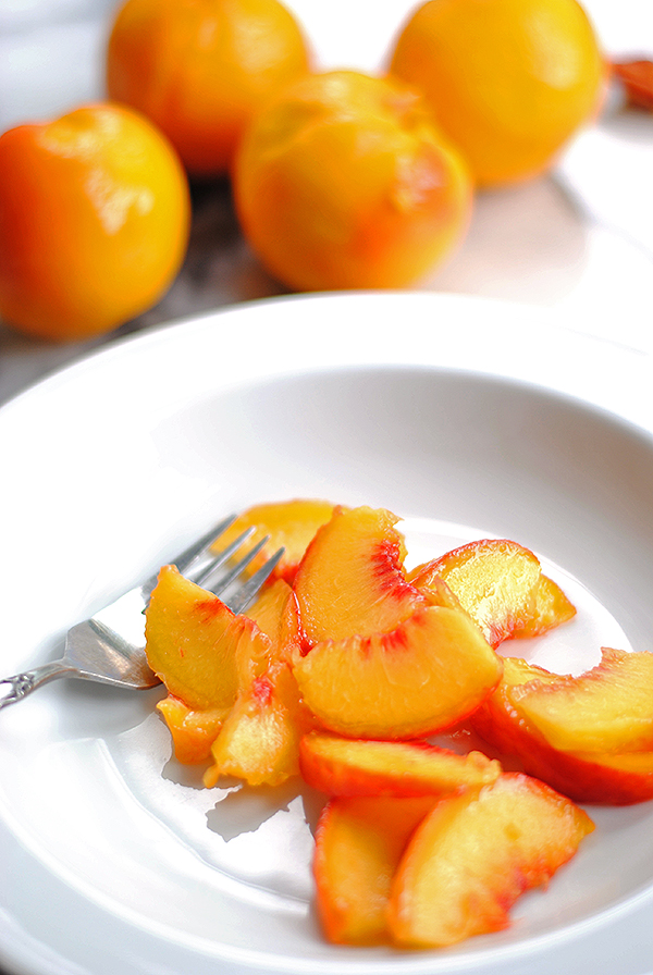 fresh peaches sliced in a white bowl with whole peaches behind