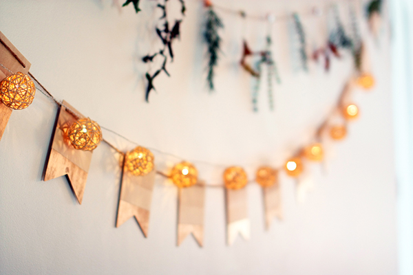 bamboo ornaments hanging with white lites, gold bunting, twigs and leaves on a white wall
