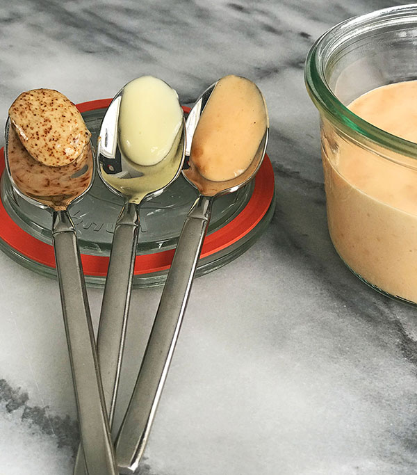 three spoons of aioli and mayonnaise sitting on marble counter next to red pepper aioli