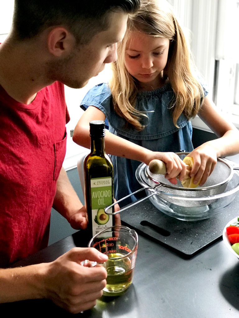 teenage boy measuring olive oil and young 5 year old girl squeezing a lemon over a bowl together