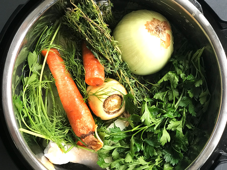 instant pot full of bone broth ingredients with carrot and onion on top
