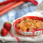 individual strawberry rhubarb almond crumbles in a white dish next to fresh rhubarb on a marble counter