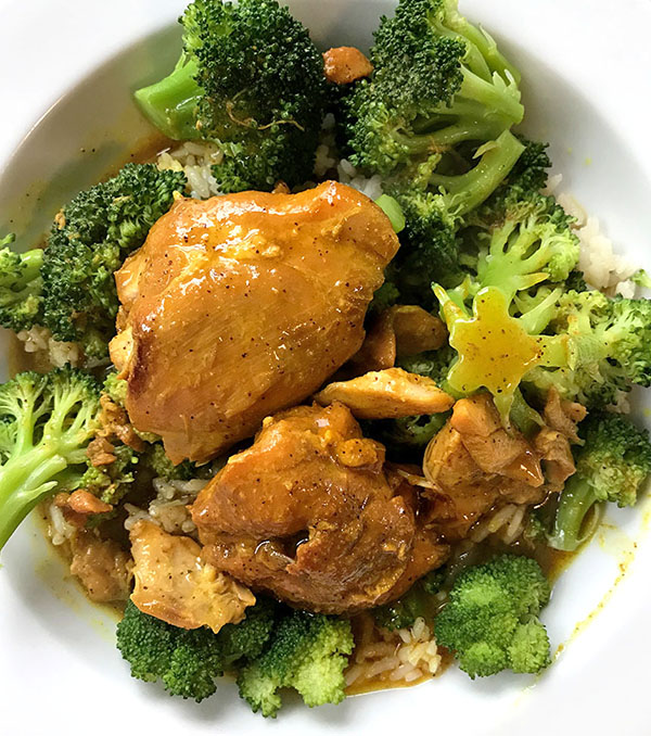 white bowl of tandoori chicken, rice and broccoli with sauce on top. 