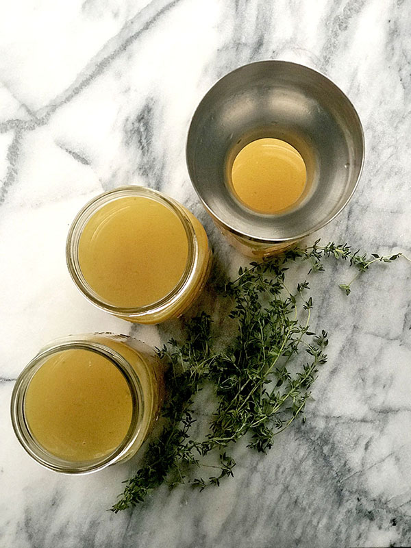 three mason jars of bone broth and one copper funnel with herbs on a counter
