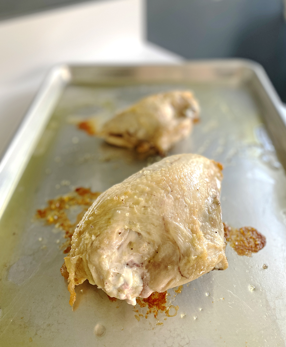 two roasted bone-in and skin-on chicken breasts cooling on a silver roasting pan ready to shred for a creamy chicken salad