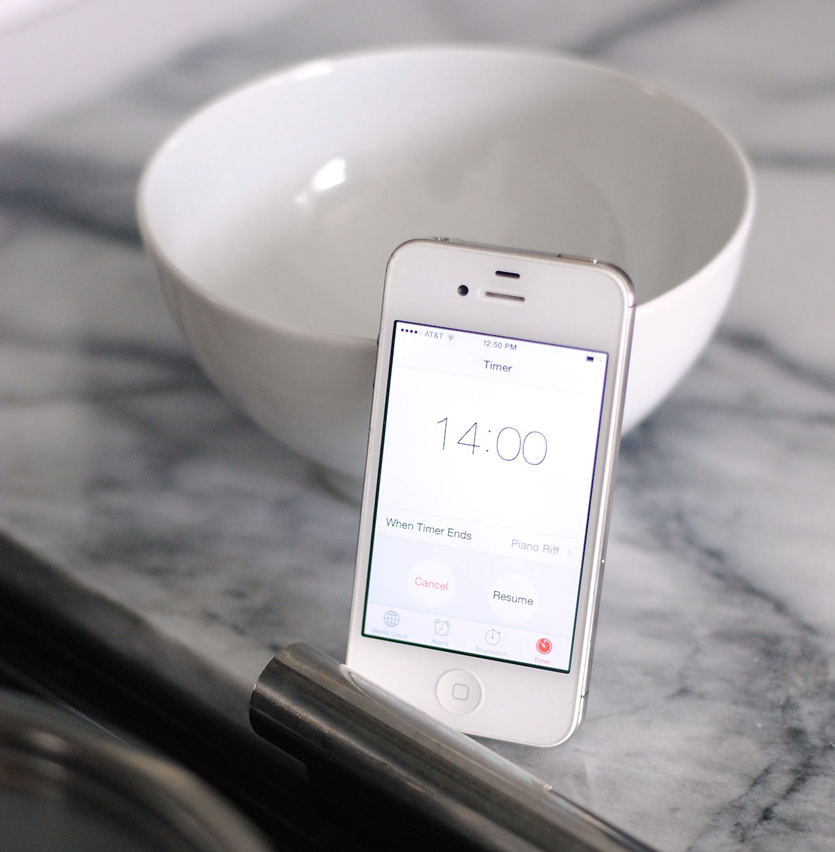Phone set to fourteen minute timer leaning on the marble counter and a white bowl. 