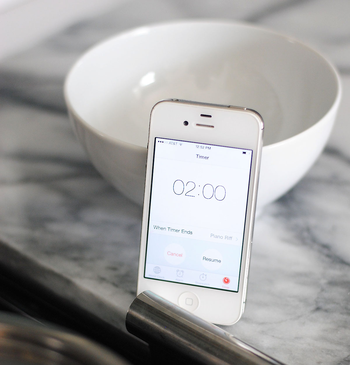 Phone timer set to two minutes leaning against a white bowl and on a marble counter. 