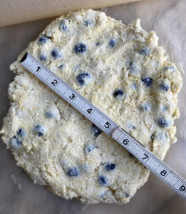scone dough pressed into seven inch diameter circle on a parchment paper pan with a measuring stick to measure