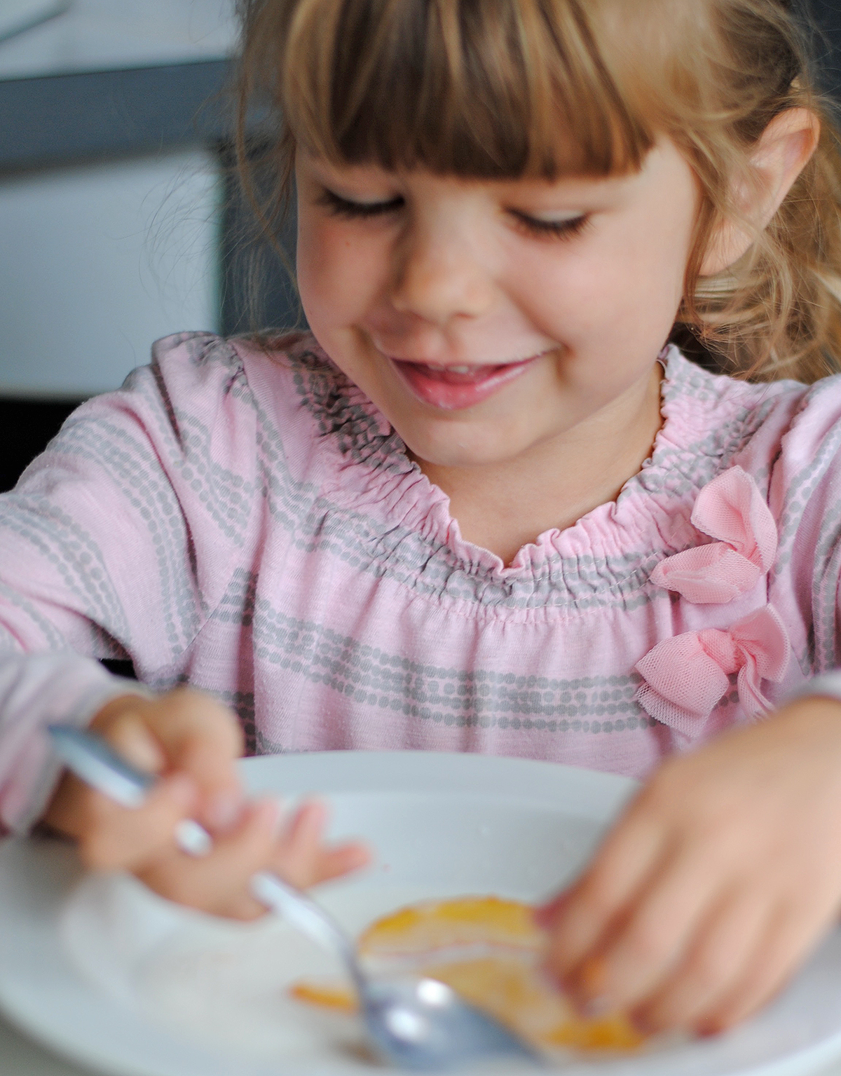 young girl dishing up a sliced peeled peach with some cream in a bowl with her hands and a spoon