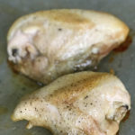 chicken breasts with skin on and bone in roasting on a pan with salt and pepper sprinkled