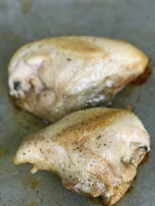 chicken breasts with skin on and bone in roasting on a pan with salt and pepper sprinkled