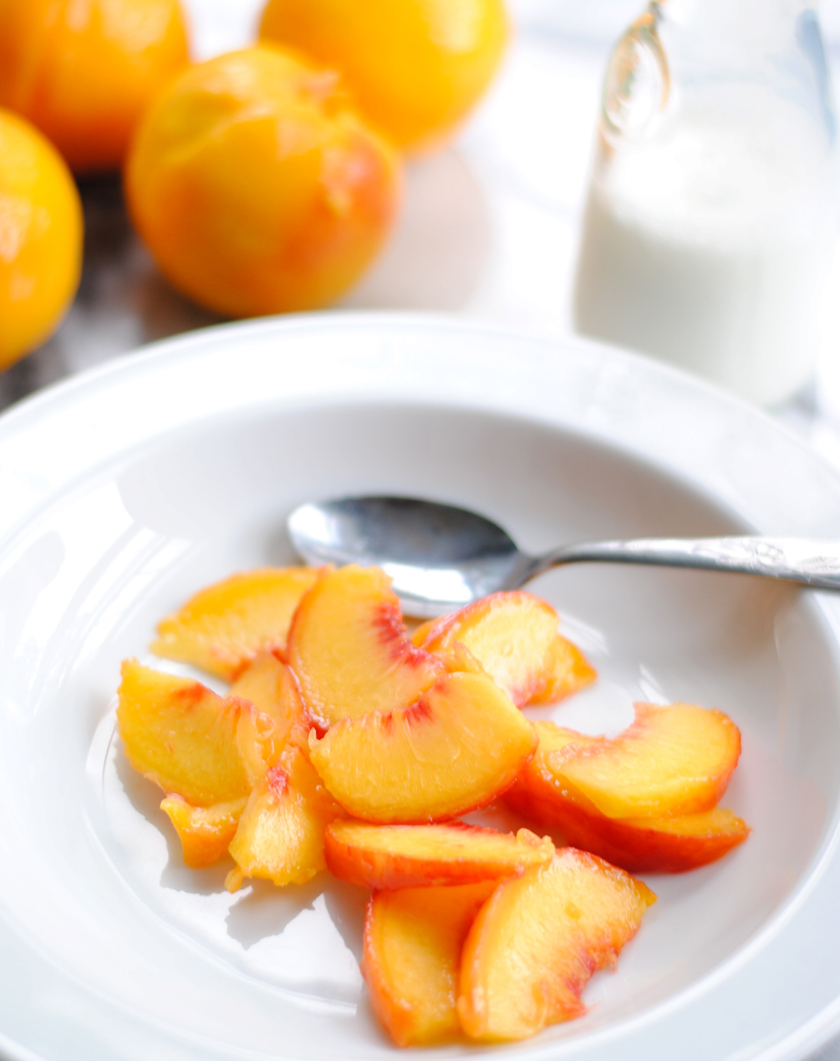 white bowl with sliced peaches and cream with spoon and cream and peaches in the background