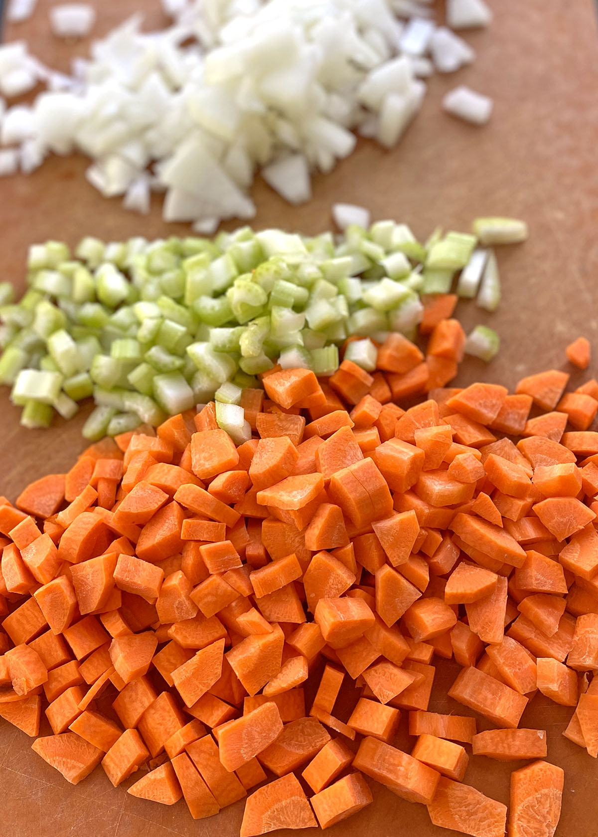 Chopped onions, celery, and carrots on a cutting board for the best chicken and wild rice soup. 