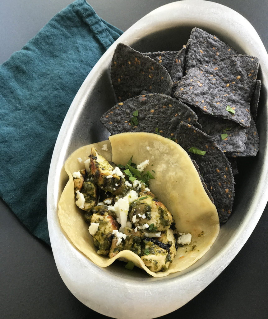 tacos and blue chips with poblano peppers in a silver dish by a teal colored napkin 