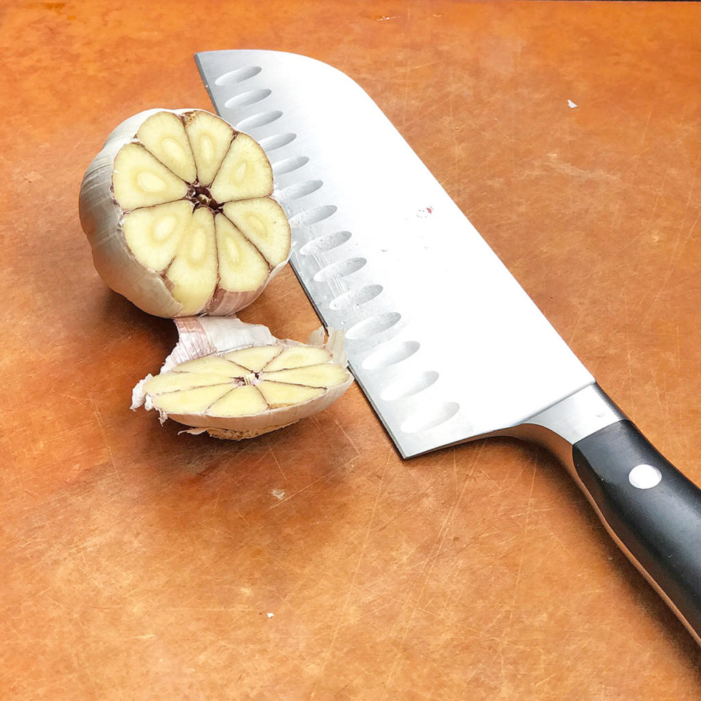 knife resting next to cut head of garlic for step one of recipe with poblano peppers
