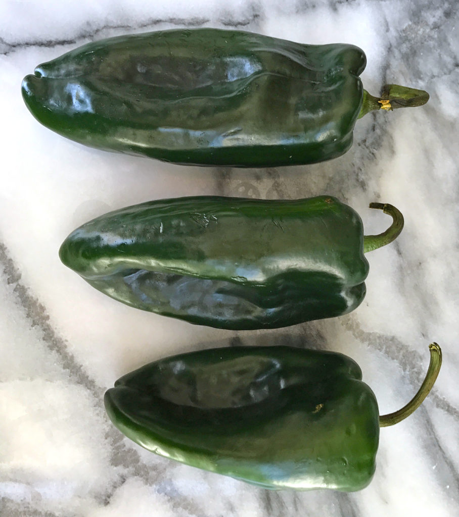 Three poblano peppers, small, medium, and large sitting on marble counter.
