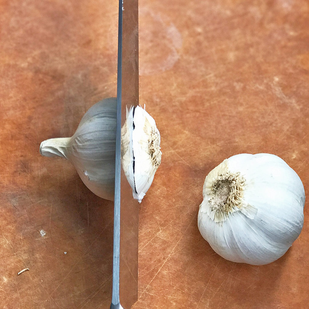 knife slicing through head of garlic for poblano peppers sauce recipe