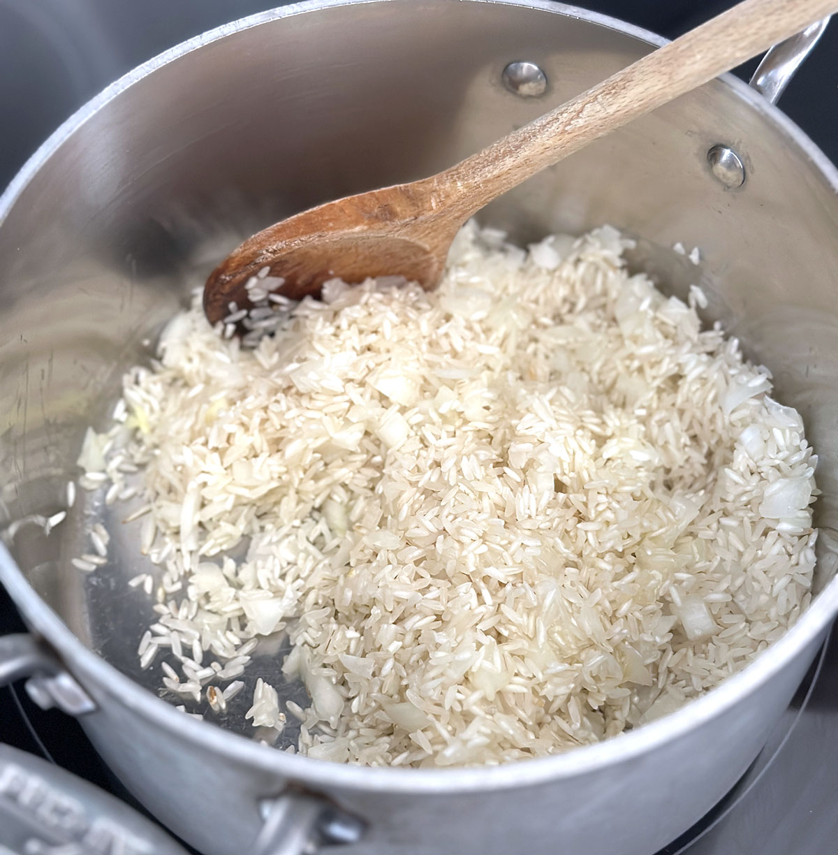 Stainless steel pot with wood spoons stirring white rice and onions.