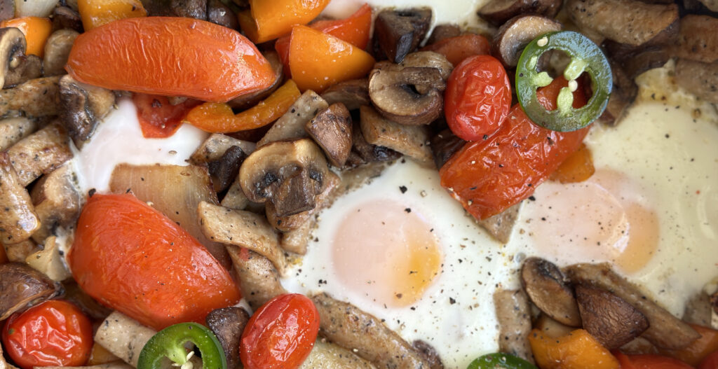 Over easy eggs with sauteed mushrooms, sausages, tomatoes, onions, and jalapenos up close.
