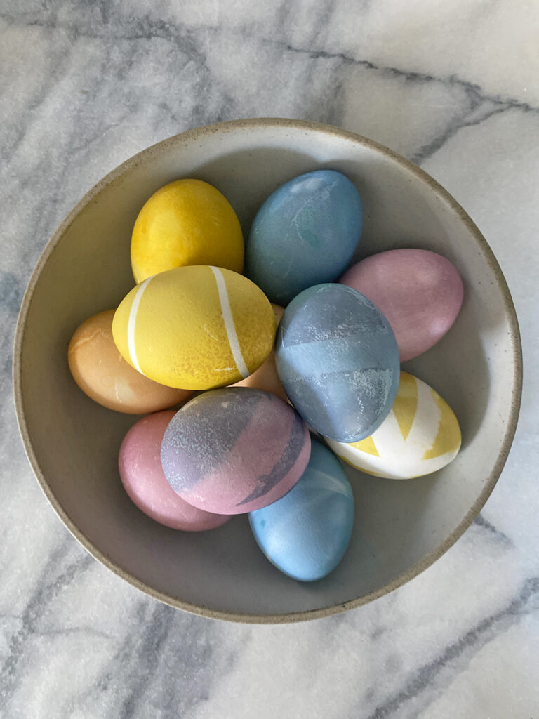 A bowl of colored eggs with food dye for Easter sitting on a marble table.