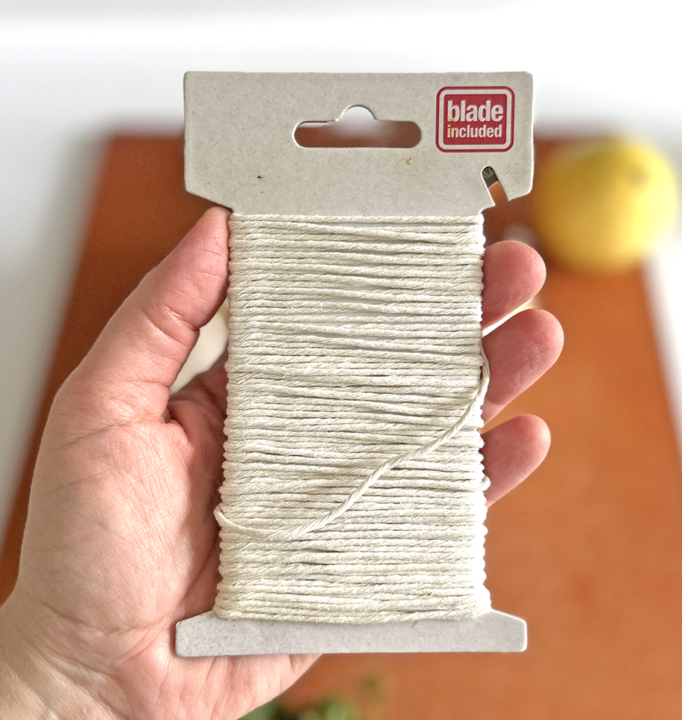 A hand holding a cardboard with white kitchen string wrapped around it for use with a top blade for cutting. 