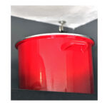 Large red shiny stockpot with silver rim sitting on a top shelf next to ceiling.