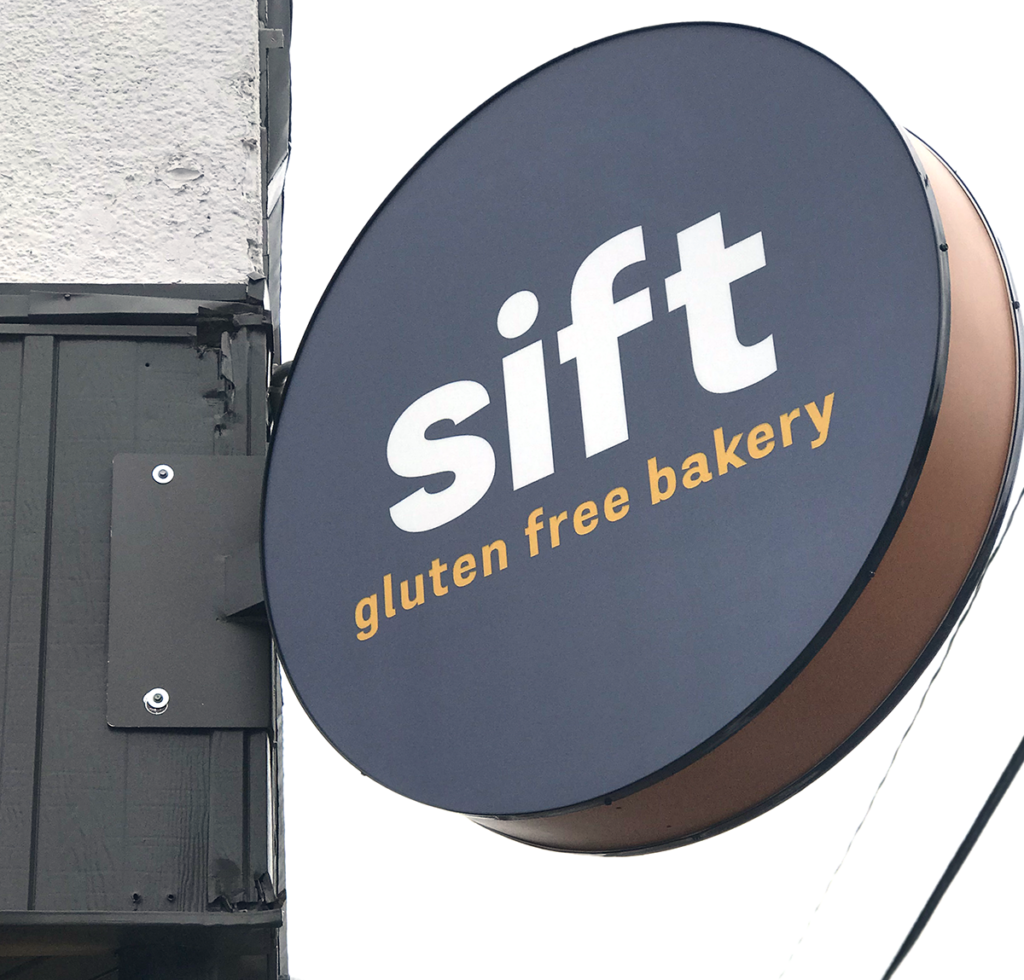 Gray round sign with whie letters that spell sift and say gluten free bakery underneath.