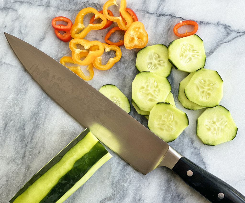 knife cutting a cucumber ond pepper pieces on a marble surface.