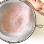 mesh strainer with blitzed powdered sugar and dried strawberries into a pink dust