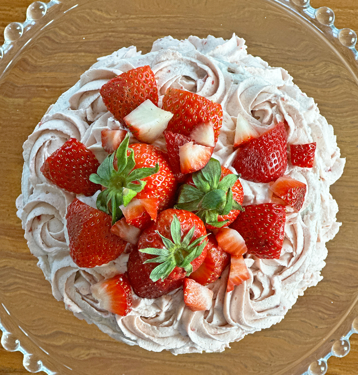 Glass plate with strawberry pink frosted round cake view from the top with fresh strawberries.