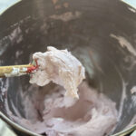 spoon of pink colored strawberry whippe coconut cream over a mixing bowl