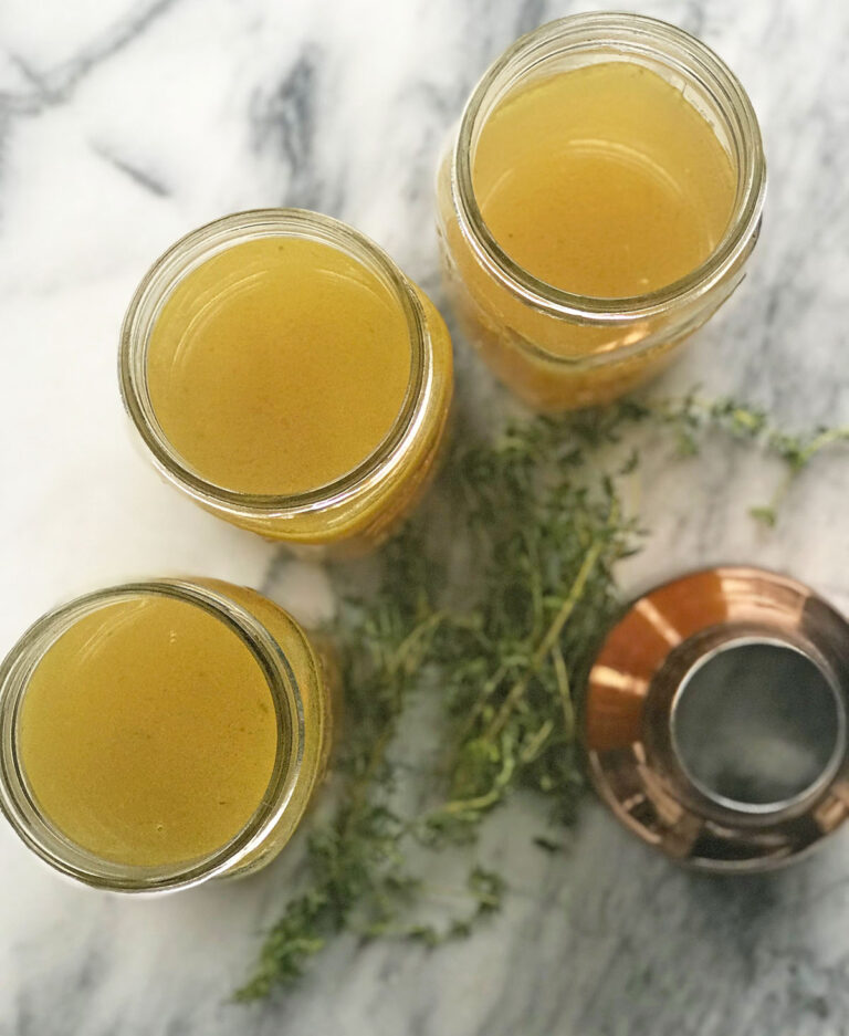 three jars of golden bone broth filled to top next to herbs and copper funnel