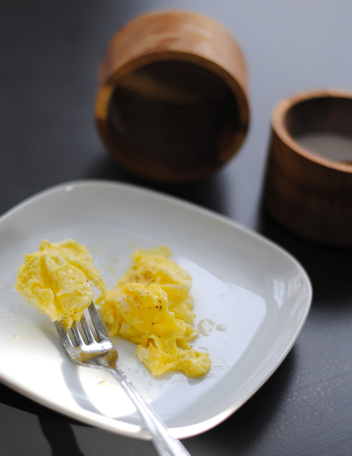 Soft scrambled eggs served on a white plate with salt and a fork