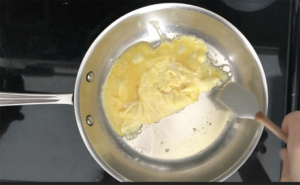 Scraping scrambled eggs in a stainless steel pan with a silicone spatula