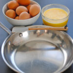 Stainless steel pan with spatula, eggs, and salt on a counter