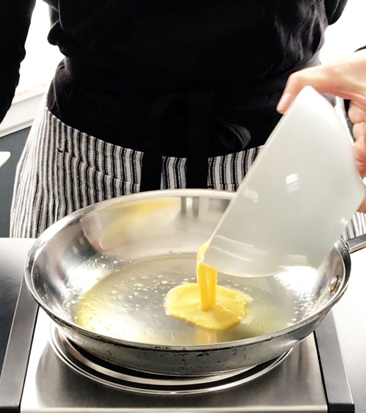 Pouring whisked eggs into a stainless steel pan to make scrambled eggs