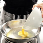 Pouring whisked eggs into a stainless steel pan to make scrambled eggs