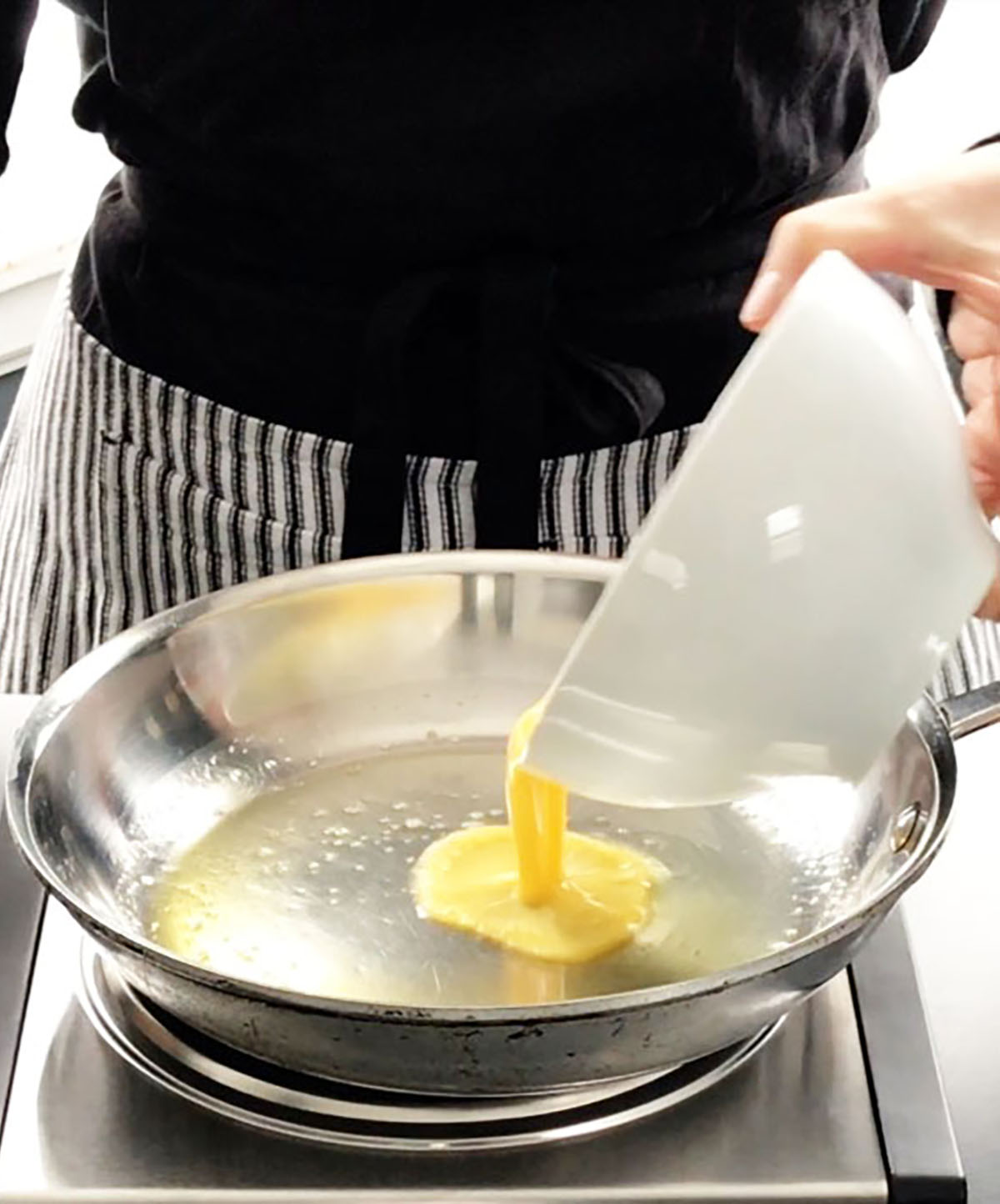 Pouring whisked eggs into a stainless steel pan to make scrambled eggs