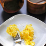 Soft scrambled eggs served on a white plate with salt and a fork