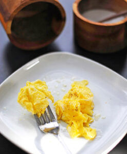 Soft scrambled eggs served on a white plate with salt and a fork