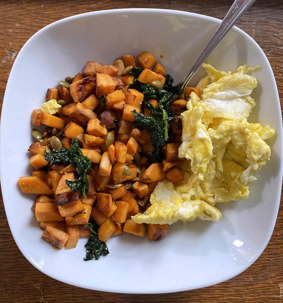 Scrambled eggs and sweet potato hash in a white bowl on rustic desk