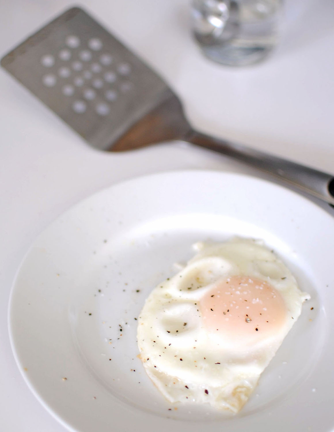 white plate with fried egg and a metal spatula sitting next to it on counter
