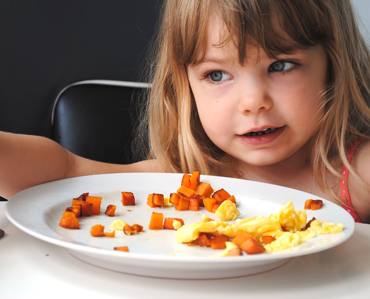 Child eating sweet potato hash at breakfast table