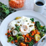 White bowl of sweet potato hash with over-easy eggs, seeds, and kale