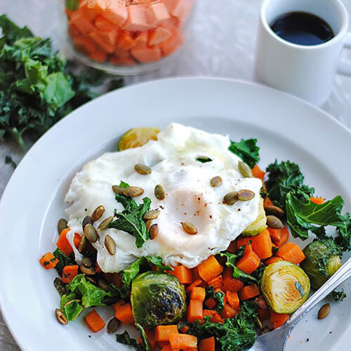 White bowl of sweet potato hash with over-easy eggs, seeds, and kale